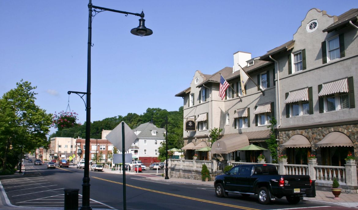an image of Bernadsville´s downtown street with some cars and in your typical houses, some that with flags in the facade